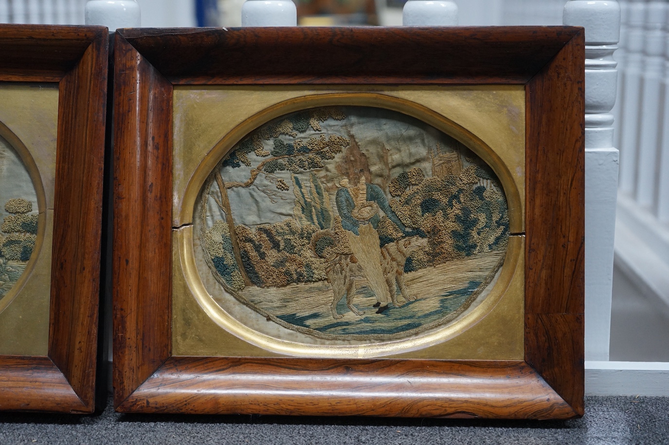 A pair of early 19th century rosewood-framed silk worked oval embroideries. Each embroidered with a boy and girl in a country landscape with their dogs. Worked in stem stitch and a knotting, the sky and faces hand painte